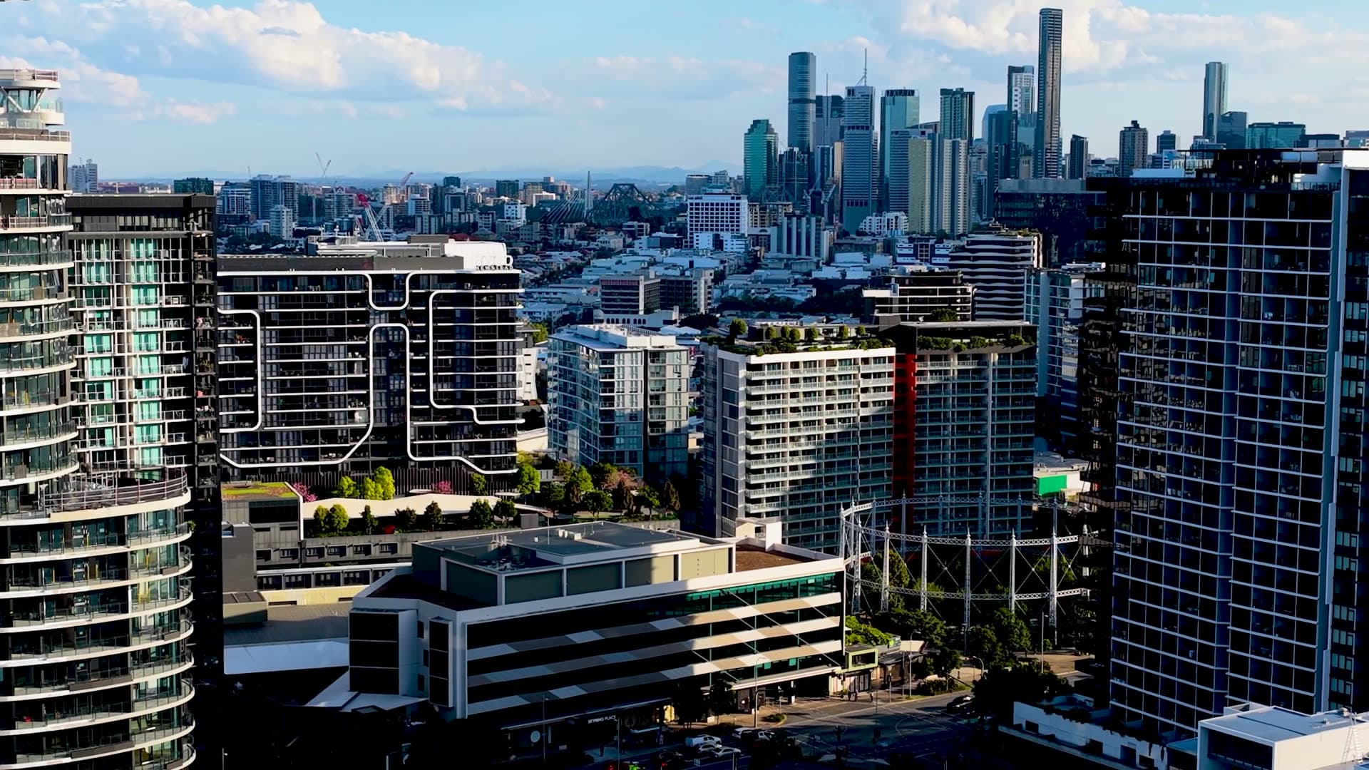 Aerial view over inner-city Brisbane apartment towers toward the CBD skyline and Story Bridge